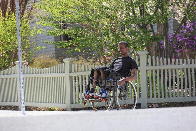 Hombre en silla de ruedas que tenía meningitis espinal en un vecindario apoyado en sus ruedas - foto de stock