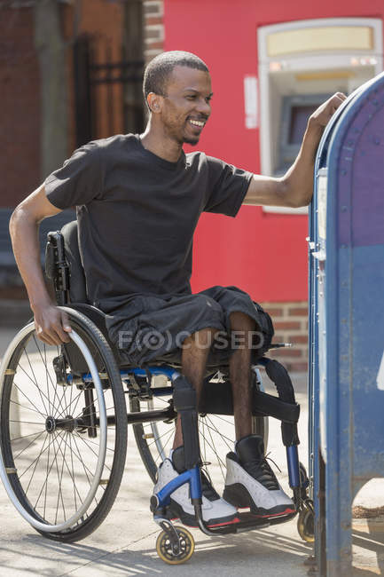 Чоловік у інвалідному візку, який мав спинний менінгіт, використовуючи поштову скриньку — стокове фото