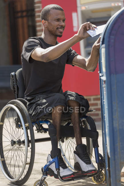 Homme en fauteuil roulant qui avait une méningite rachidienne mettre une lettre dans une boîte aux lettres publique — Photo de stock