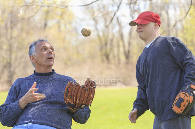 Padre con lesión en la médula espinal e hijo con síndrome de Down a punto de jugar béisbol en el parque - foto de stock