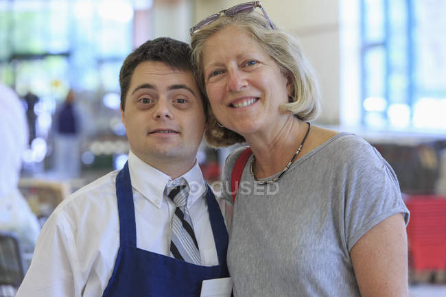Hombre con Síndrome de Down trabajando en una tienda de comestibles y abrazándose con la mujer - foto de stock