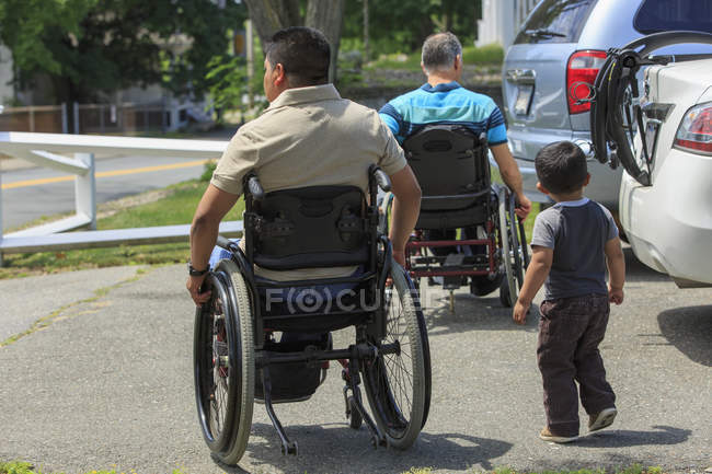 Друзья с травмами спинного мозга в инвалидных колясках с ребенком на парковке — стоковое фото