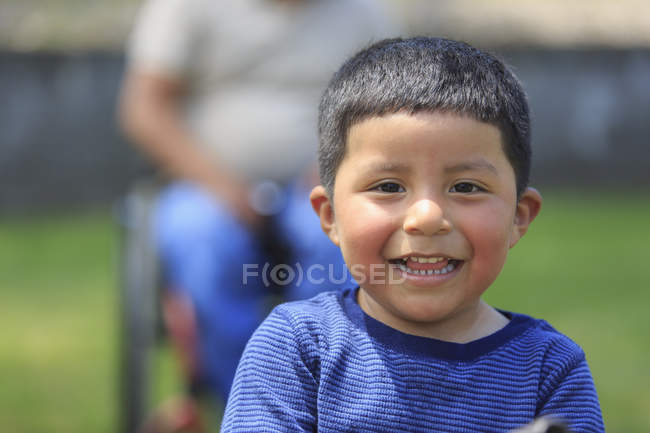 Счастливый портрет латиноамериканца с отцом в инвалидной коляске с травмой спинного мозга на заднем плане — стоковое фото