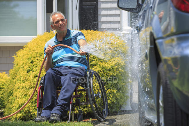 Человек с травмой спинного мозга в инвалидном кресле моет свою доступную машину — стоковое фото