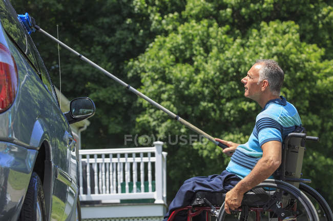 Человек с травмой спинного мозга в инвалидном кресле моет свою доступную машину — стоковое фото