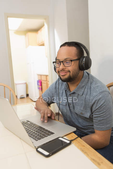 Happy African American man with Down Syndrome listening to music with headphones at home and using laptop — Stock Photo