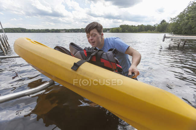 Молодой человек с синдромом Дауна готовится использовать байдарку в озере — стоковое фото
