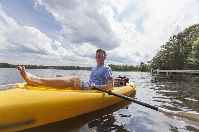 Счастливый молодой человек с синдромом Дауна катается на байдарке по озеру — стоковое фото