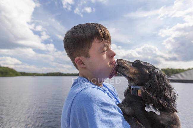 Young man with Down Syndrome playing with a dog on a dock — Stock Photo