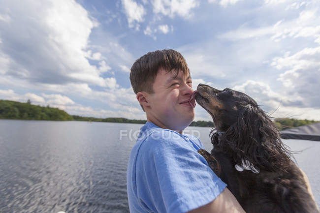 Giovane con la sindrome di Down che gioca con un cane su un molo — Foto stock