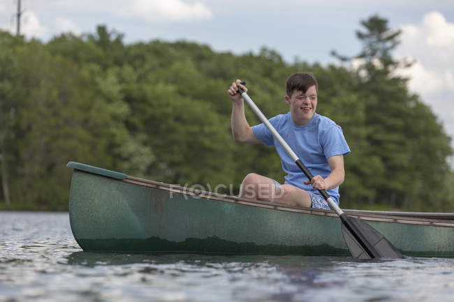 Молодой человек с синдромом Дауна гребёт на каноэ в озере — стоковое фото
