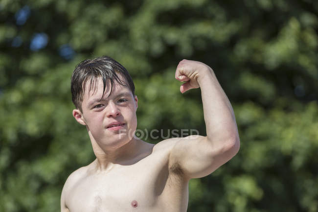 Портрет молодого человека с синдромом Дауна, показывающего свой бицепс на причале — стоковое фото