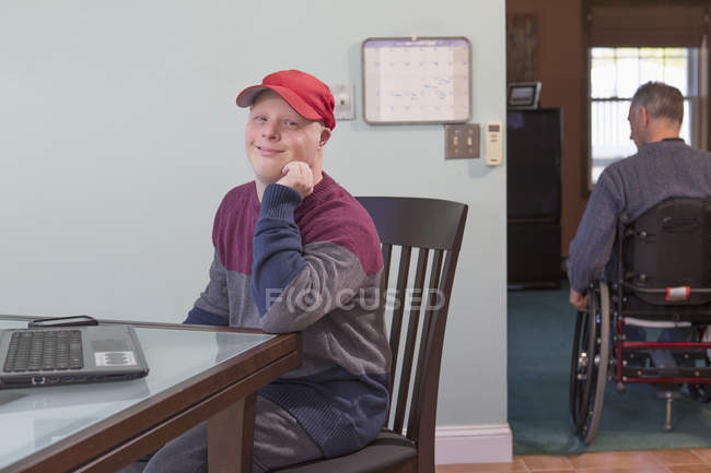 Padre con lesión de médula espinal e hijo con síndrome de Down con computadora portátil en casa - foto de stock