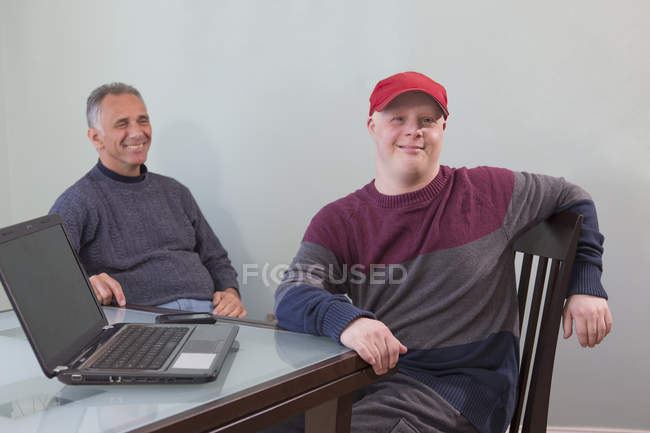 Padre con lesione del midollo spinale e figlio con sindrome di Down con computer portatile a casa — Foto stock
