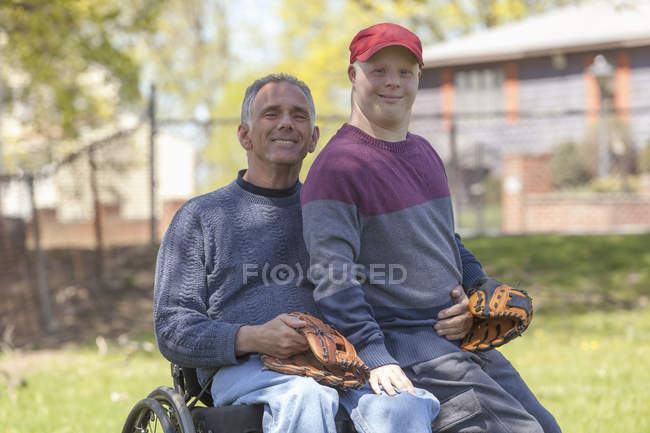 Padre con lesión en la médula espinal e hijo con síndrome de Down a punto de jugar béisbol en el parque - foto de stock
