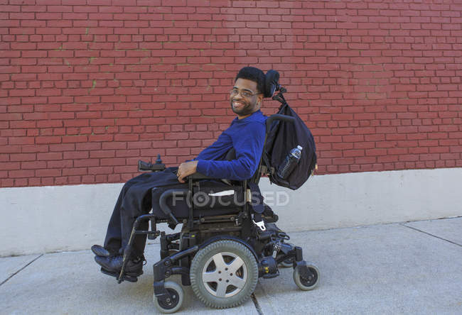 Heureux homme afro-américain atteint de paralysie cérébrale en utilisant son fauteuil roulant électrique à l'extérieur — Photo de stock