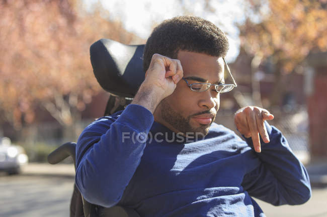African American man with Cerebral Palsy putting on eyeglasses on his power wheelchair outside — Stock Photo