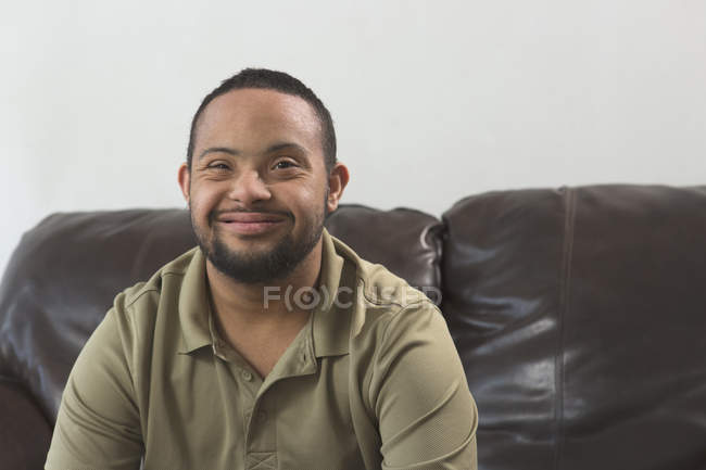 Щасливий афроамериканець людина з синдромом Дауна сидячи на дивані будинку — стокове фото