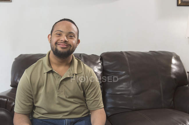 Щасливий афроамериканець людина з синдромом Дауна сидячи на дивані будинку — стокове фото