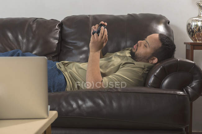 Hombre afroamericano feliz con síndrome de Down usando el controlador de juego en casa - foto de stock