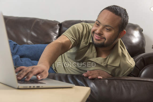 Homem afro-americano feliz com síndrome de Down usando laptop em casa — Fotografia de Stock