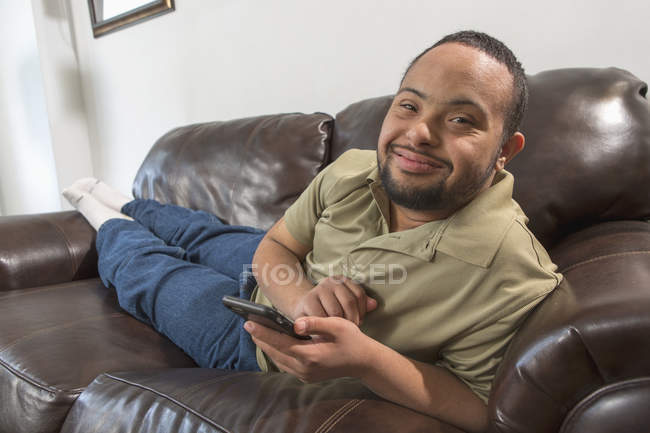 Glücklicher afrikanisch-amerikanischer Mann mit Down-Syndrom zu Hause mit Smartphone — Stockfoto