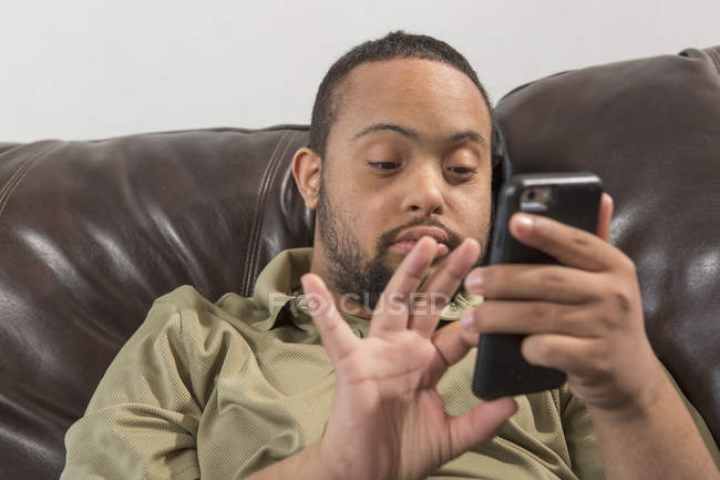 Happy African American man with Down Syndrome using smartphone at home — Stock Photo