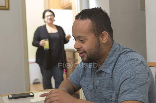 Щасливий афроамериканець людина з синдромом Дауна за допомогою ноутбука з матір'ю вдома — стокове фото