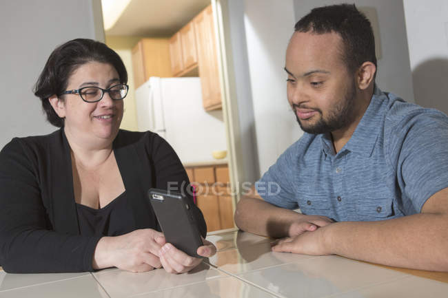 Happy African American man with Down Syndrome with mother using smartphone at home — Stock Photo