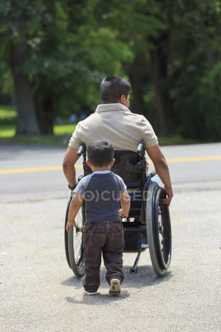 Homem hispânico com lesão medular em cadeira de rodas com seu filho — Fotografia de Stock