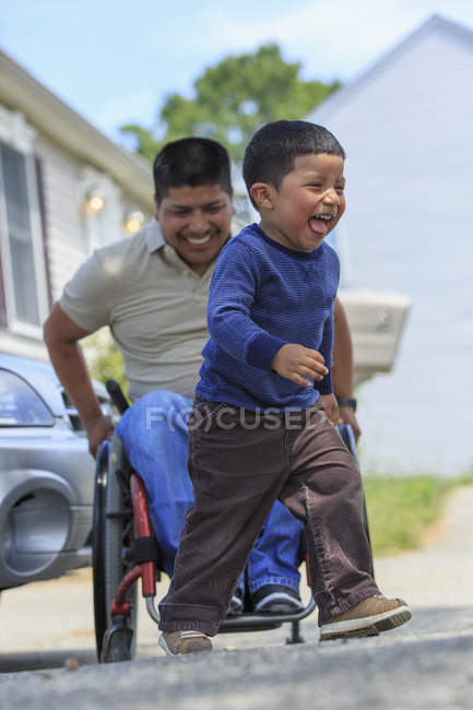 Spanischer Mann mit Querschnittslähmung im Rollstuhl spielt mit seinem Sohn — Stockfoto