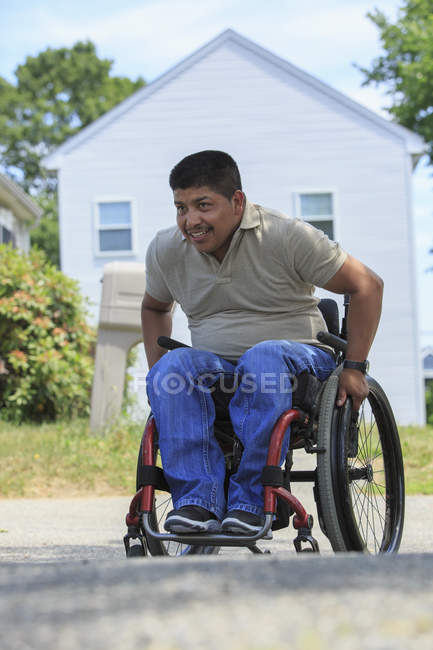 Hombre hispano con lesión de médula espinal en silla de ruedas frente a su casa - foto de stock