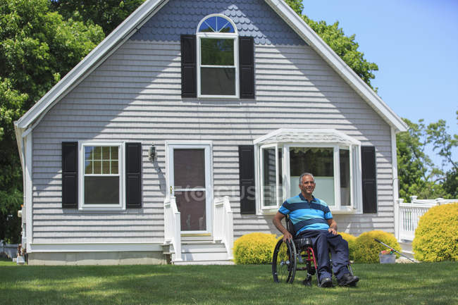 Человек с травмой спинного мозга в инвалидной коляске перед своим домом — стоковое фото