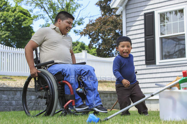 Spanischer Mann mit Querschnittslähmung im Rollstuhl mit seinem Sohn beim Waschen eines Autos — Stockfoto