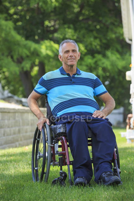 Портрет счастливого человека с травмой спинного мозга в инвалидном кресле на газоне — стоковое фото