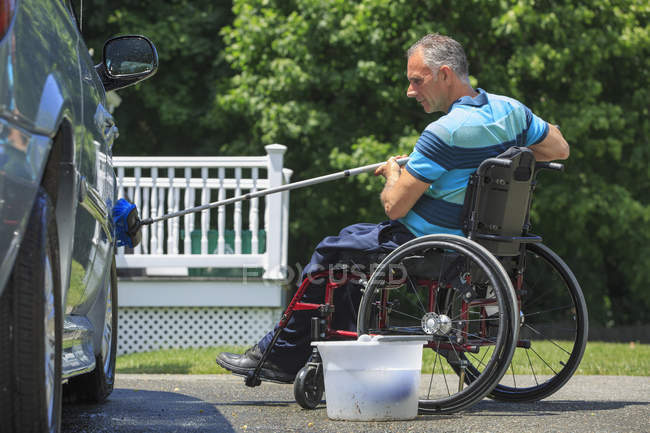 Чоловік з травмою спинного мозку в інвалідному візку миє свій доступний автомобіль — стокове фото