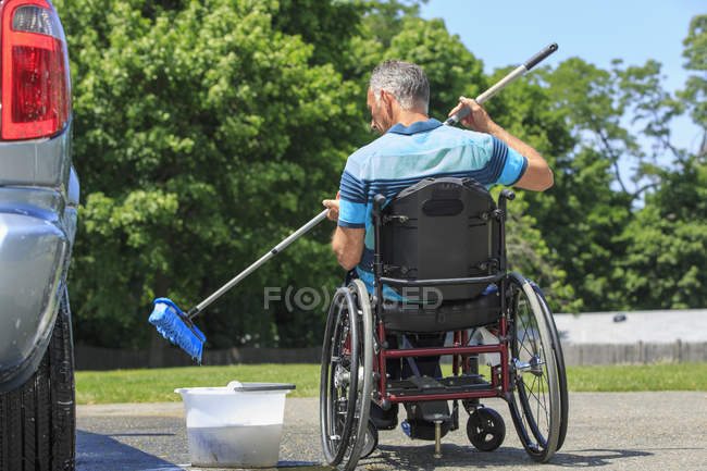 Homem com uma lesão medular na cadeira de rodas lavando seu carro acessível — Fotografia de Stock