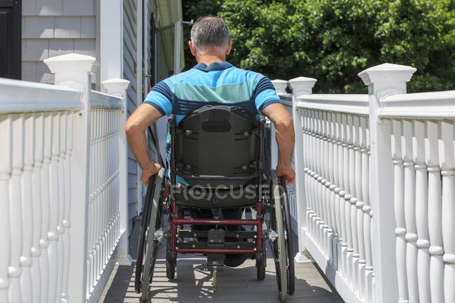 Человек с травмой спинного мозга в инвалидной коляске входит в пандус своего дома — стоковое фото