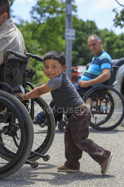 Uomo ispanico con lesione del midollo spinale in sedia a rotelle con suo figlio — Foto stock