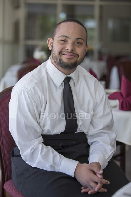 Retrato de un hombre afroamericano feliz con síndrome de Down como camarero en un restaurante - foto de stock