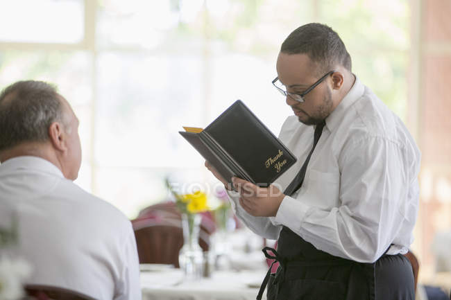Афроамериканець людина з синдромом Дауна як офіціант приймаючи замовлення від клієнта в ресторані — стокове фото