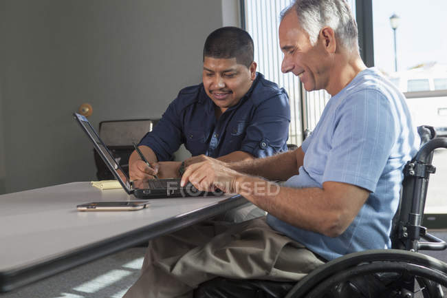 Двое мужчин с травмами спинного мозга работают в офисе — стоковое фото