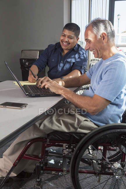 Двое мужчин с травмами спинного мозга работают в офисе — стоковое фото