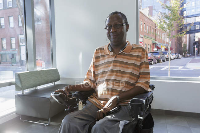 Человек с синдромом Гийена-Барре на инвалидной коляске перед окном квартиры — стоковое фото