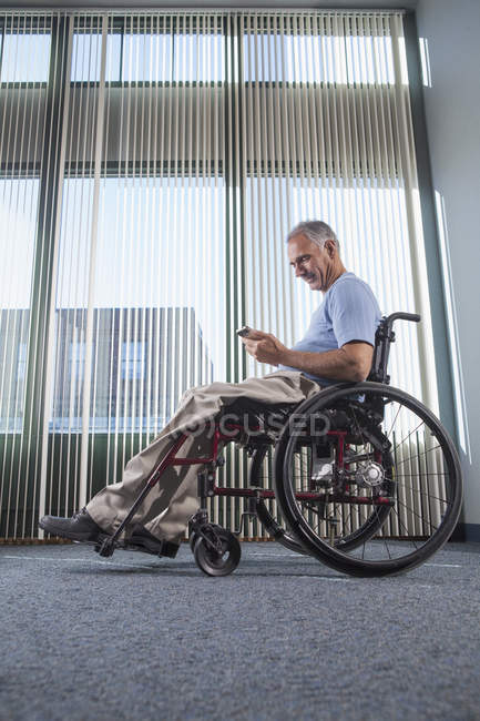 Uomo con lesione del midollo spinale sulla sedia a rotelle utilizzando il telefono in un corridoio dell'ufficio — Foto stock