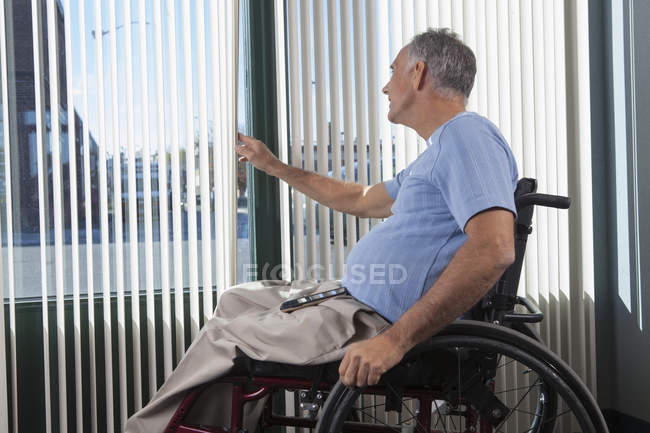 Mann mit Querschnittslähmung im Rollstuhl schaut aus Bürofenster — Stockfoto