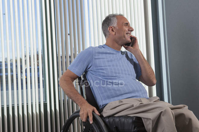 Человек с травмой спинного мозга в инвалидном кресле разговаривает по телефону в офисе — стоковое фото