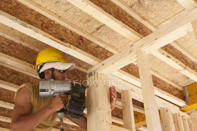 Carpinteiro usando uma pistola de prego em uma moldura de parede — Fotografia de Stock