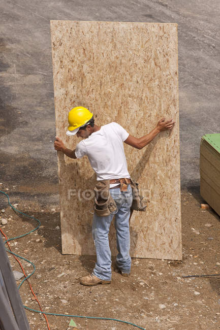 Hispanic carpenter carrying a floor panel at a house under construction — Stock Photo