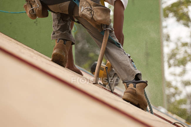 Charpentier hispanique utilisant une scie circulaire sur le panneau de toit d'une maison en construction — Photo de stock